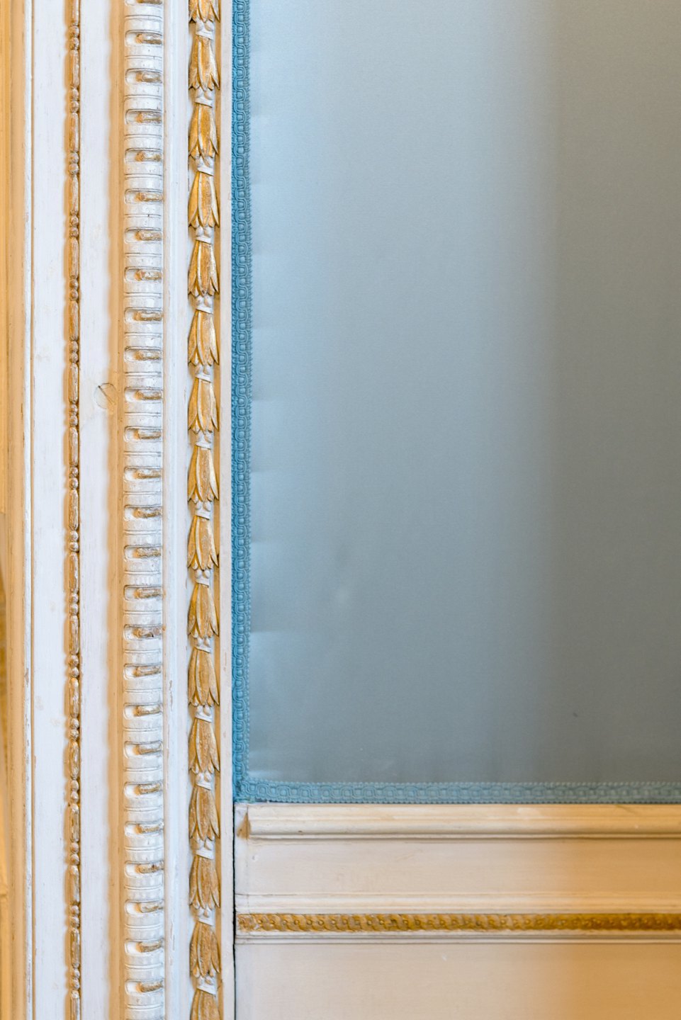 Modanature bianche e ornate con accenti dorati accanto a un pannello blu con finiture.