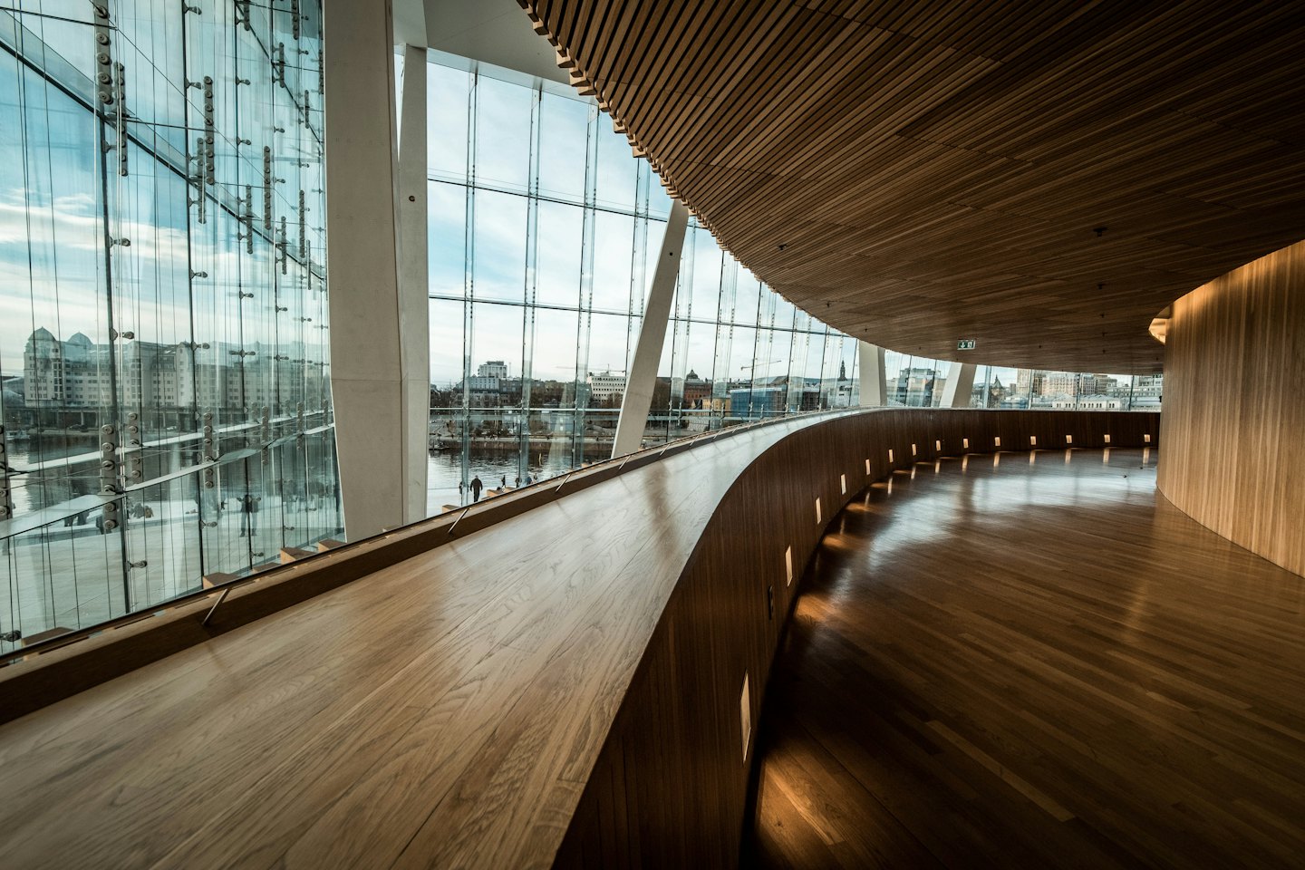 Un corridoio curvo in legno conduce a finestre che si affacciano sullo skyline di una città.