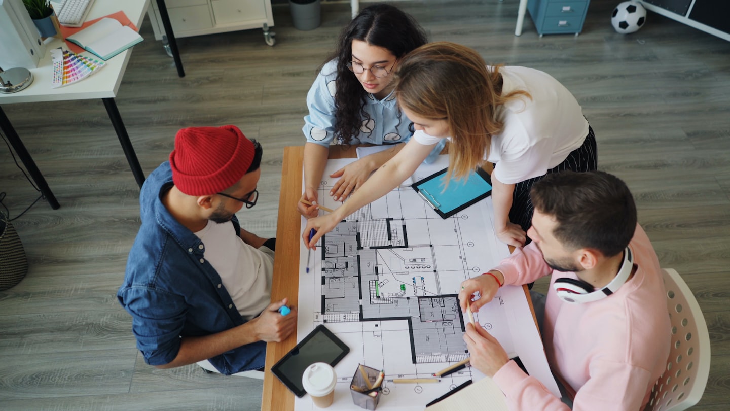 Quattro designer collaborano su un progetto architettonico su un tavolo.