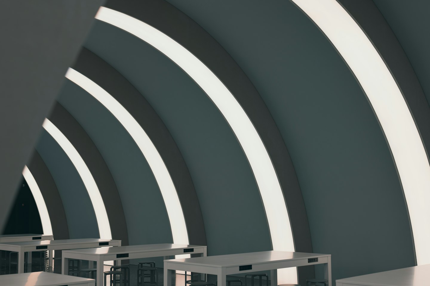 Pareti curve con illuminazione a strisce e tavoli bianchi in uno spazio di coworking moderno.